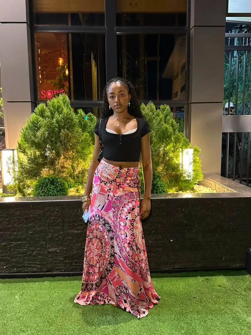 Femme en crop top noir et longue jupe fluide à motifs roses, en tenue de soirée
